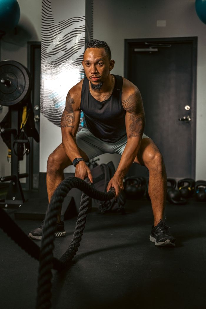 services-01 A muscular man exercises with battling ropes in a gym for strength training.