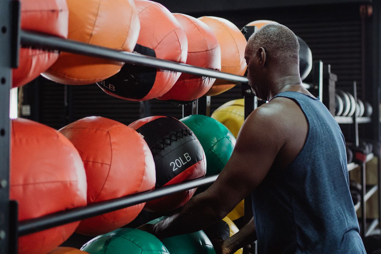 about-us-01 Athletic man selecting a 20-pound medicine ball for his fitness routine in a modern gym setting.